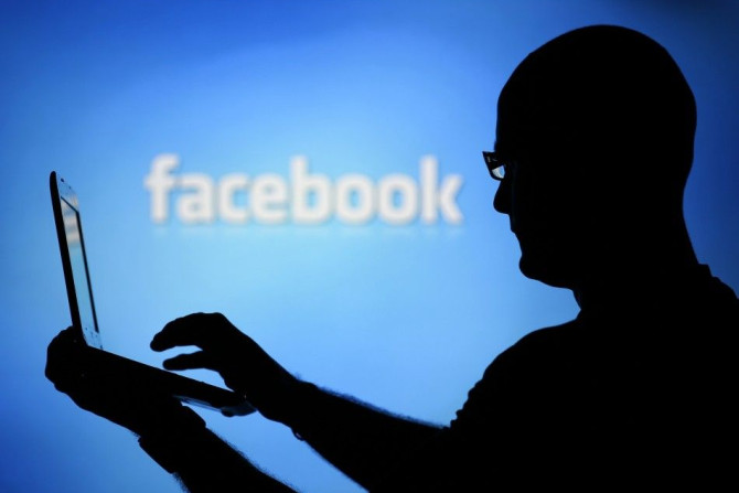 A man is silhouetted against a video screen with an Facebook logo 