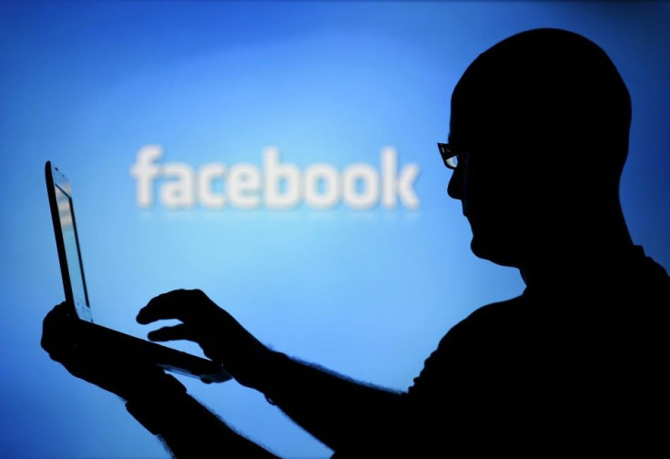 A man is silhouetted against a video screen with an Facebook logo 