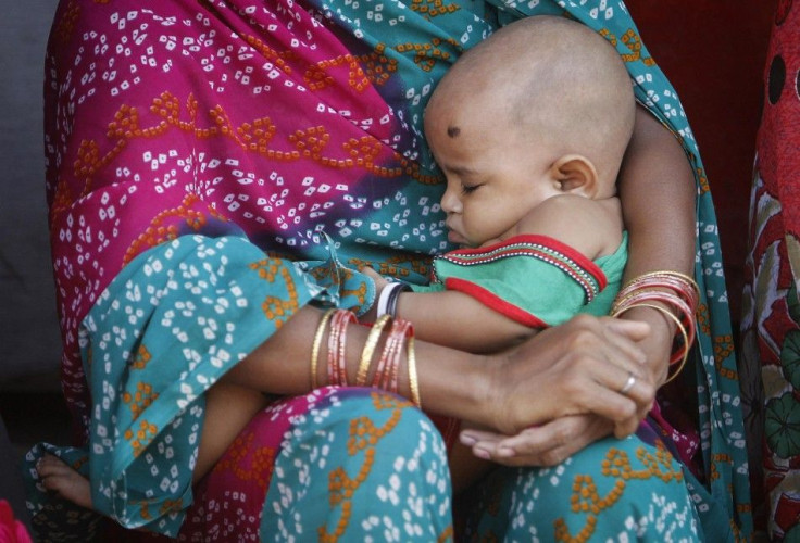 A woman holding her baby sits in a street at a slum in Mumbai