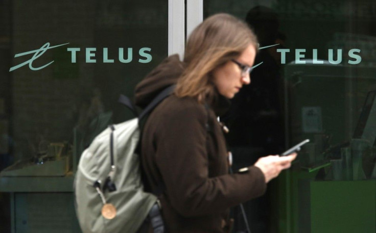 A woman uses a mobile device while walking past a Telus store in Ottawa February 19, 2014. Canadian telecom companies have paid a combined C$5.27 billion ($4.78 billion), a record high amount, to secure licenses for prime airwaves on which they plan to bu