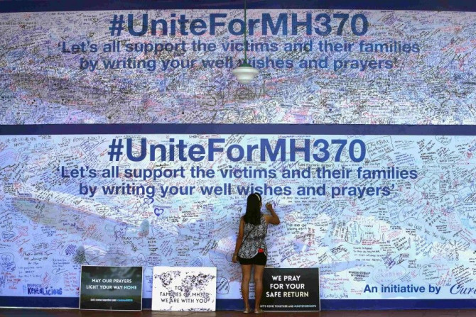 A woman writes a message on a board dedicated to passengers onboard the missing Malaysia Airlines Flight MH370 and their family members, in Petaling Jaya