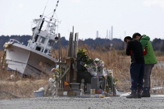 People pray for victims of the March 11, 2011 earthquake and tsunami as Tokyo Electric Power Co's (TEPCO) tsunami-crippled Fukushima Daiichi nuclear power plant is seen in the background at Namie town, Fukushima prefecture March 11, 2014. Tuesday mar