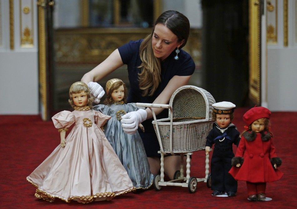 Exhibition curator Anna Reynolds poses with dolls and a wicker toy pram belonging to Britains Queen Elizabeth and her sister Princess Margaret, at Buckingham Palace in London