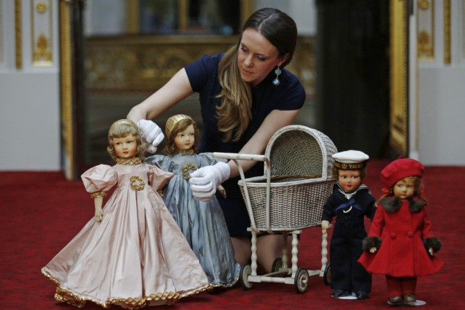 Exhibition curator Anna Reynolds poses with dolls and a wicker toy pram belonging to Britain's Queen Elizabeth and her sister Princess Margaret, at Buckingham Palace in London