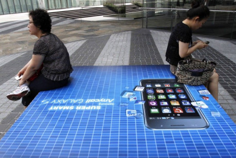 File picture shows people holding their mobile phones as they sit on an advertisement of Samsung Electronics' Galaxy S smartphone in Seoul