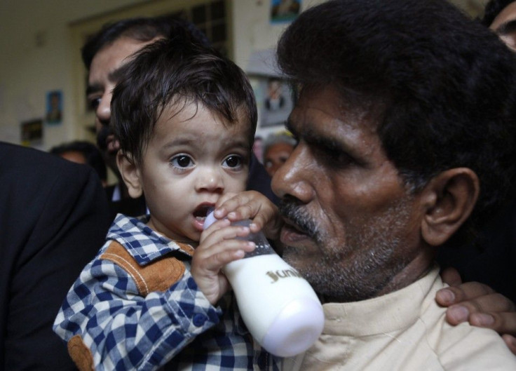 Nine-month-old baby Musa Khan drinks milk from his bottle while being carried by his grandfather Muhammad Yasin as they leave after appearing in a court in Lahore April 12, 2014. REUTERS/Mohsin Raza