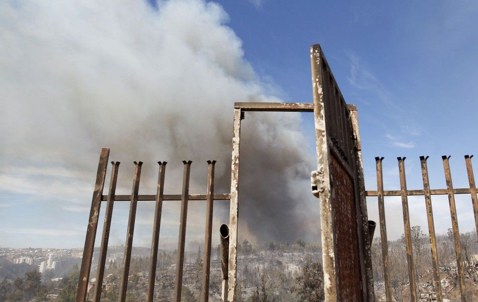 Smoke is seen through the burnt-out remains of a gate after a forest fire burned several neighbourhoods in the hills in Valparaiso city, northwest of Santiago, April 13, 2014. At least 11 people were killed and 500 houses destroyed over the weekend by the