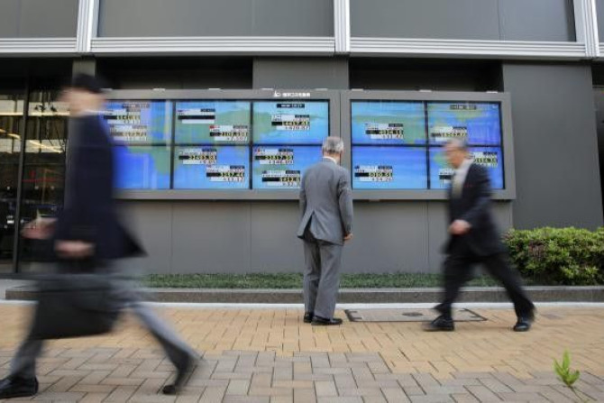 A man looks at an electronic board displaying Japan's Nikkei average (top C) and various countries' stock indices, as passers-by walk past outside a brokerage in Tokyo April 16, 2014.