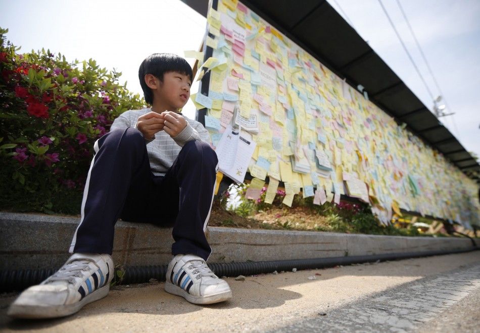 A boy sits next to a board with messages written for victims of sunken passenger ship Sewol, outside the official memorial altar in Ansan May 2, 2014. A culture of cosy personal ties that can blur the lines between businesses and those regulating them, of