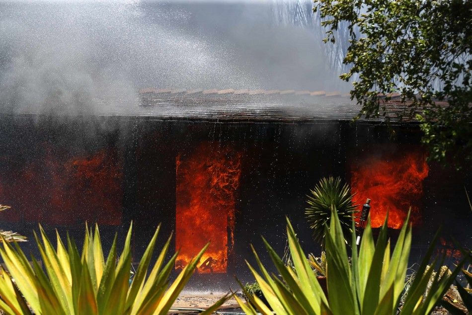 A burning home is doused with water as firefighters battle with wildfires in Carlsbad, California May 14, 2014. More than 11,000 homes and businesses were ordered to evacuate on Wednesday and power was cut off to many residents as a wind-lashed wildfire r