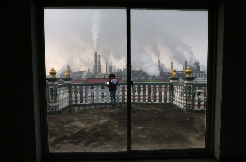 A girl reads a book on her balcony as smoke rises from chimneys of a steel plant, on a hazy day in Quzhou, Zhejiang province in this April 3, 2014 file photo. The Beijing municipal government has proposed new rules that will set tight restrictions on offs