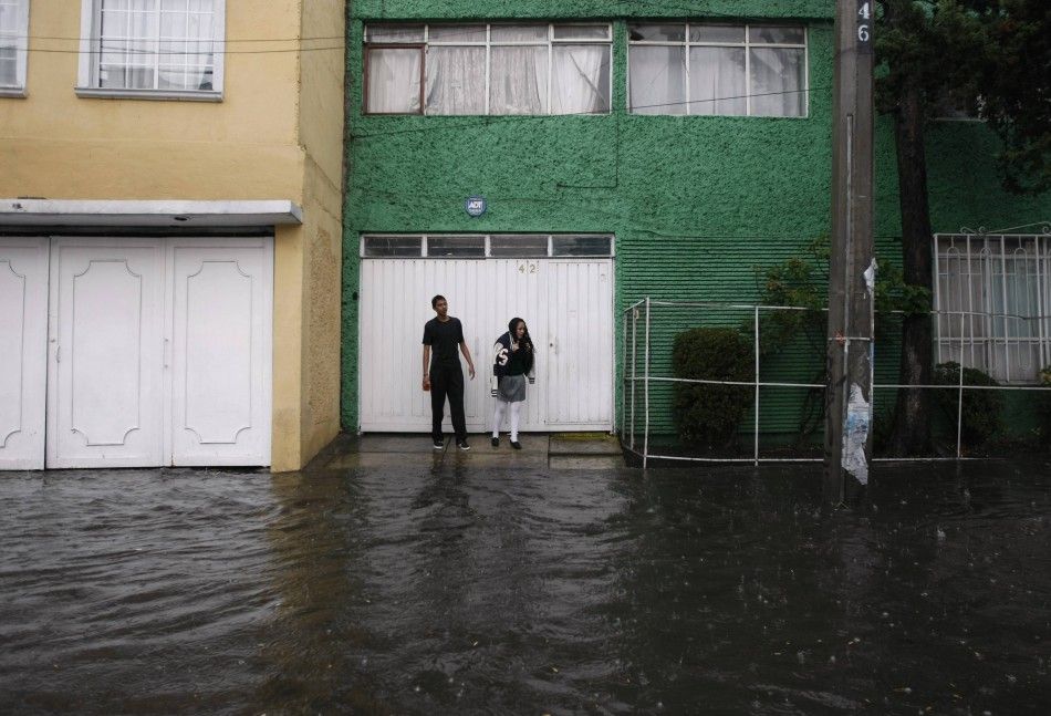 People stand on a sidewalk as they look at a flooded street after torrential rains hit several neighborhoods in Mexico City May 26, 2014. Hurricane Amanda, the first named storm of the Pacific season, moved on Monday losing strength against Mexicos Pacif