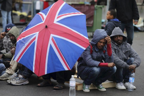 Eritrean migrants take cover from the rain under an umbrella during the daily food distribution at the harbour in Calais, northern France, May 27, 2014. French authorities dispense medicine against scabies and announced that they will close three such cam