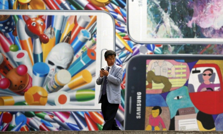 A Man Uses His Mobile Phone in Front of a Giant Advertisement Promoting Samsung New Galaxy S5 Smartphone, at an Art Hall in Central Seoul
