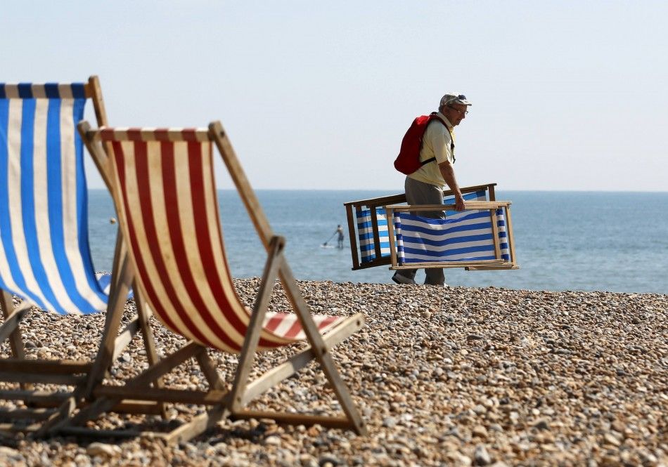 A Man Carries Deckchairs to Sit in the Sun on Brighton Beach in Southern England