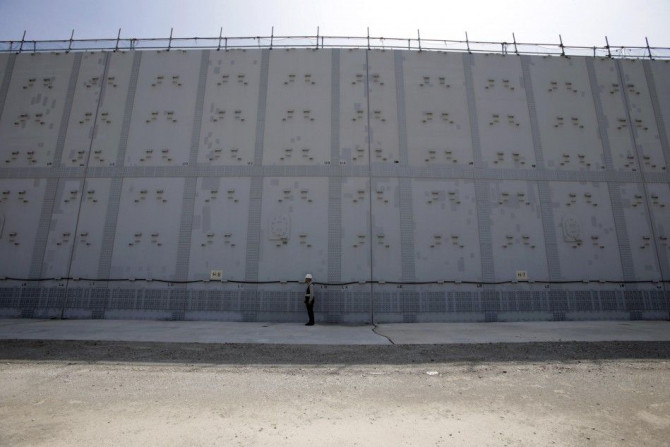A worker stands in front of an 18-m (59-ft) high and 1.6-km (1-mile) long tsunami defence wall at Chubu Electric Power Co.'s Hamaoka Nuclear Power Station in Omaezaki, Shizuoka Prefecture, in this file picture taken May 17, 2013. In the three years since 