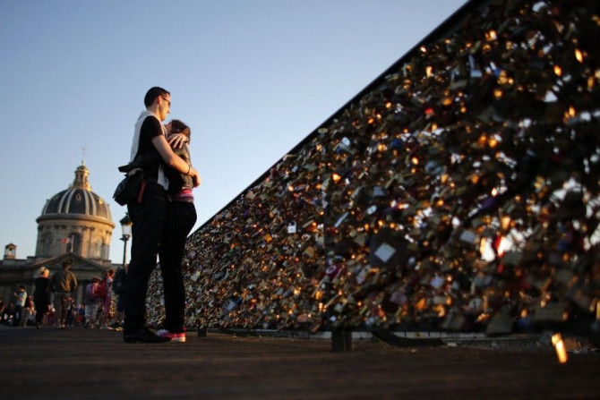 A couple embraces during sunset on the Pont des Arts with its fence covered with padlocks clipped by lovers over the River Seine in Paris, in this August 10, 2013 file photo. The Pont des Arts footbridge over the Seine in central Paris was closed for a fe