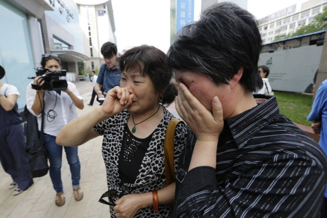 A woman (L), whose son, daughter-in-law and grandson were aboard the missing Malaysia Airlines flight MH370, cries after she and other family members failed to express their appeals to the airline outside its office in Beijing June 11, 2014. Months of sea