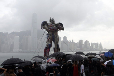 Reporters hold umbrellas under a 21-foot tall model of the Transformers character Optimus Prime during heavy rain before the world premiere of the film &quot;Transformers: Age of Extinction&quot; in Hong Kong June 19, 2014.