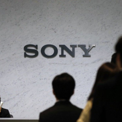 A Receptionist Speaks On A Phone Under A Sony Corp Logo.