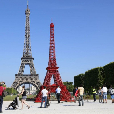 People stop to observe a replica of the Eiffel Tower built with red bistro chairs to mark the 125th anniversary of the Fermob company&#039;s bistro chairs in Paris