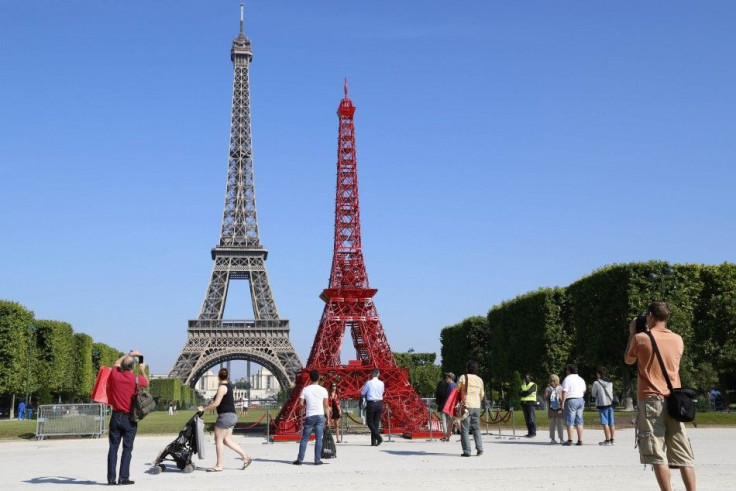 People stop to observe a replica of the Eiffel Tower built with red bistro chairs to mark the 125th anniversary of the Fermob company&#039;s bistro chairs in Paris