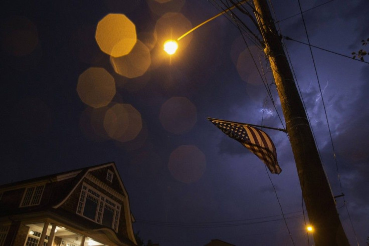 American flag is seen blowing in wind as lightning brightens raindrops in the sky along Main Street in Port Washington, New York