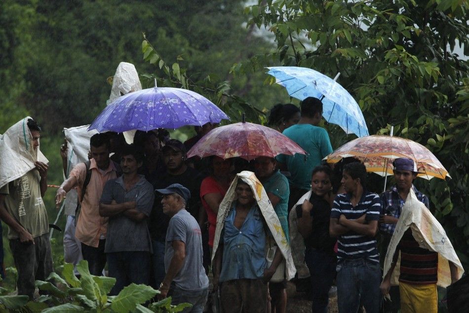 Miners and residents take cover from rain under umbrellas at the site of a landslide at a gold mine in San Juan Arriba, outskirts of Tegucigalpa July 3, 2014. Rescuers labored with pickaxes and shovels to dig out 11 miners trapped by a landslide at an ill