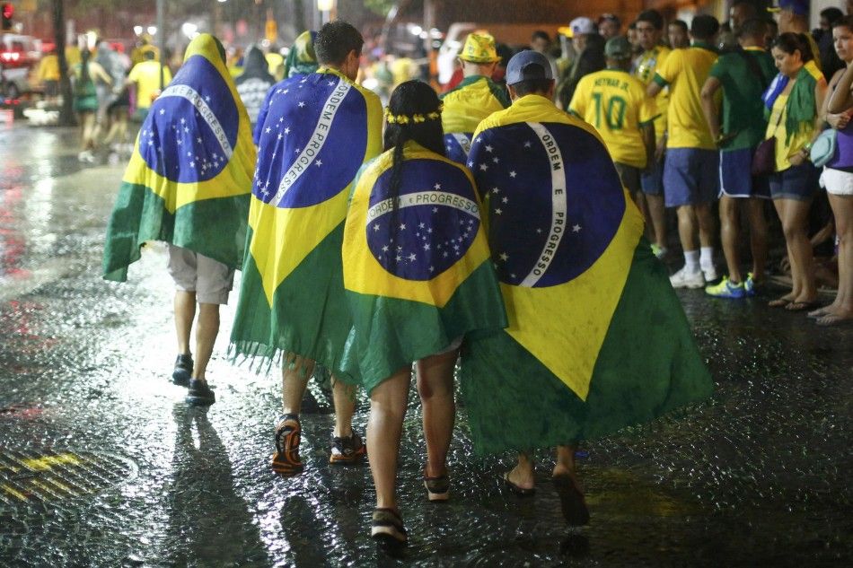 Brazil soccer fans walk in the rain after watching a broadcast of their teams loss against Germany in their 2014 World Cup semi-final match in Rio de Janeiro