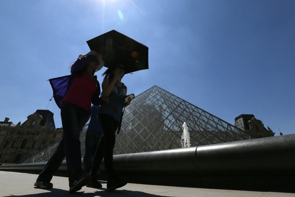 Tourists use a umbrella to protect themselves from the sun walk near the Pyramid entrance of the Louvre Museum on a hot summer day in Paris July 3, 2014.  REUTERSGonzalo Fuentes FRANCE - Tags TRAVEL ENVIRONMENT TPX IMAGES OF THE DAY