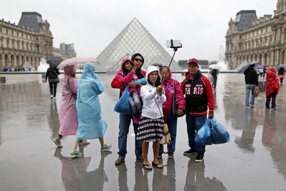 Tourists take a selfie near the Pyramid of the Louvre Museum on a rainy summer day in Paris July 9, 2014.    REUTERSCharles Platiau FRANCE - Tags ENVIRONMENT TRAVEL TPX IMAGES OF THE DAY