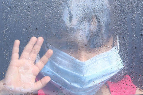 A girl wearing a mask looks out a car window as rain drops are seen in Taif