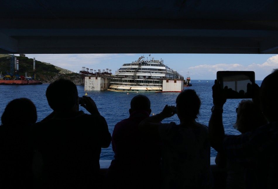 Tourists take a pictures from a ferry boat of the capsized cruise liner Costa Concordia as they arrive outside Giglio harbour July 13, 2014. The refloat operation for Costa Concordia is expected to begin on July 14 and be completed on July 21.  REUTERSAl