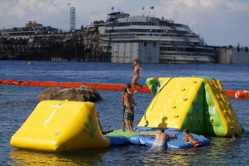 People dive in front of the cruise liner Costa Concordia at Giglio harbour, Giglio Island July 13, 2014. Italian authorities gave the green light to refloating the wrecked Costa Concordia cruise ship on Saturday, setting the stage for the next step in the