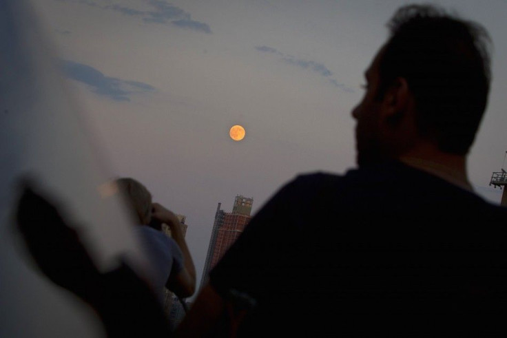 A man is reflected in a car window as he looks at the moon one day ahead of the Supermoon phenomenon from a bridge over 42nd St. in the Manhattan borough of New York