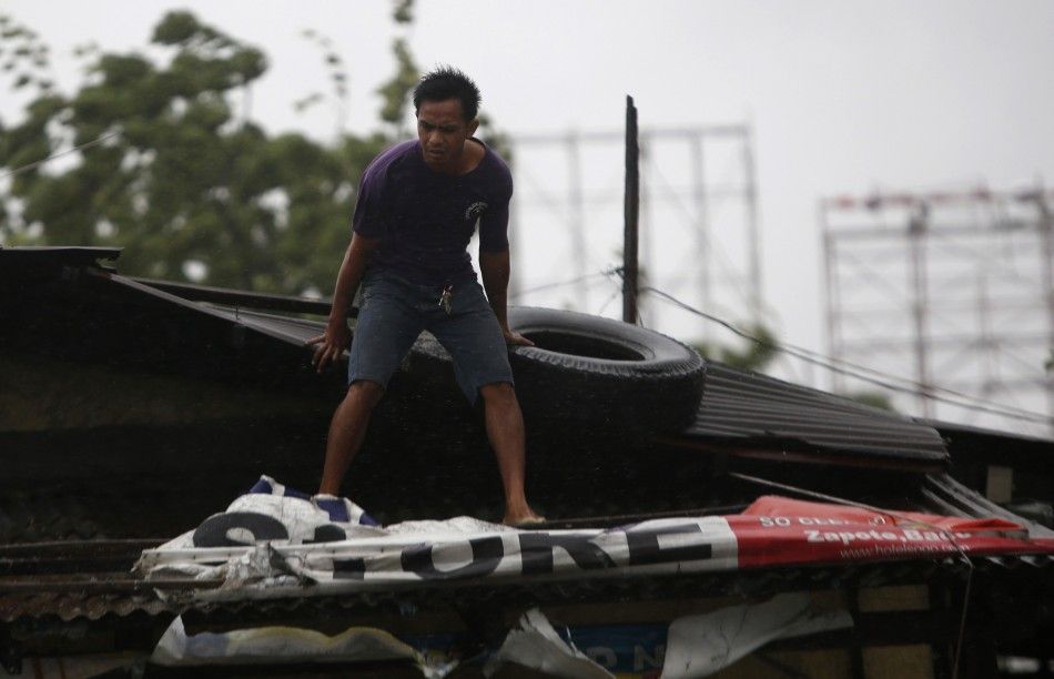 A man places a tire on the roof of his house as Typhoon Rammasun locally named Glenda hit the town of Imus, Cavite southwest of Manila, July 16, 2014. Philippine authorities evacuated almost 150,000 people from their homes and shuttered financial market