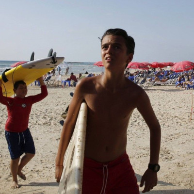 Boys carry their surf boards ashore after their lesson was cancelled following a mid-air explosion from a rocket which was intercepted by the Iron Dome defense system, in Tel Aviv