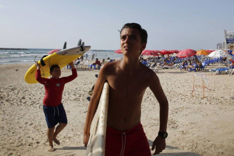 Boys carry their surf boards ashore after their lesson was cancelled following a mid-air explosion from a rocket which was intercepted by the Iron Dome defense system, in Tel Aviv