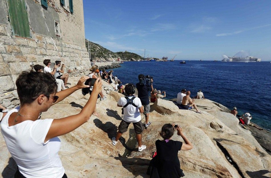 People takes pictures abd watch the cruise liner Costa Concordia during the refloat operation maneuvers at Giglio Island July 23, 2014. Maneuvers began early on Wednesday to remove the rusty hulk of the Costa Concordia cruise liner from the Italian island