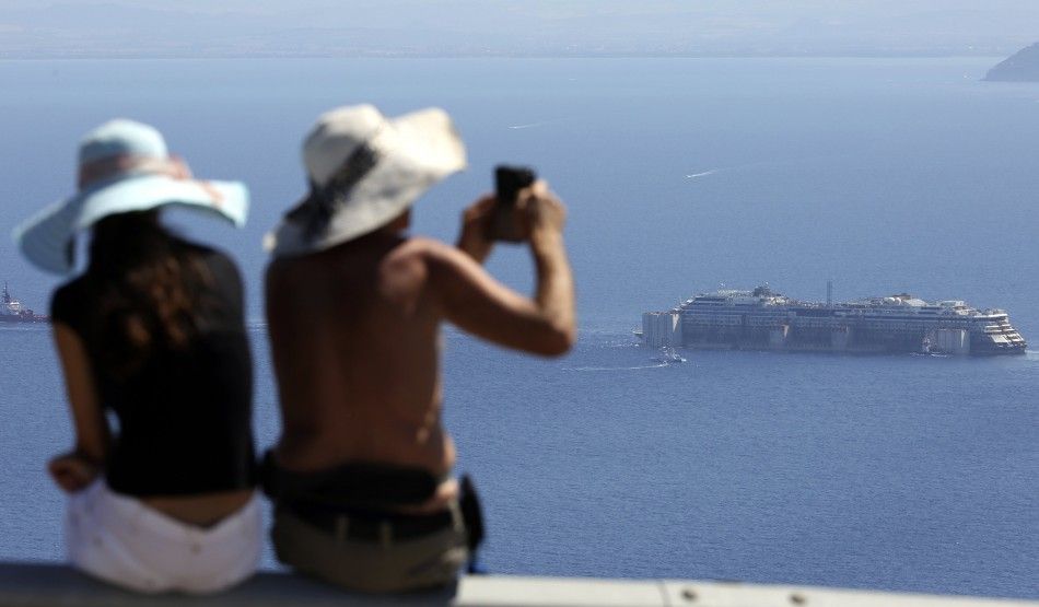 A woman takes a picture of the cruise liner Costa Concordia after it left Giglio Island July 23, 2014. The rusty hulk of the Costa Concordia cruise liner began its journey to the scrapyard on Wednesday after a two-year salvage operation off the Italian is