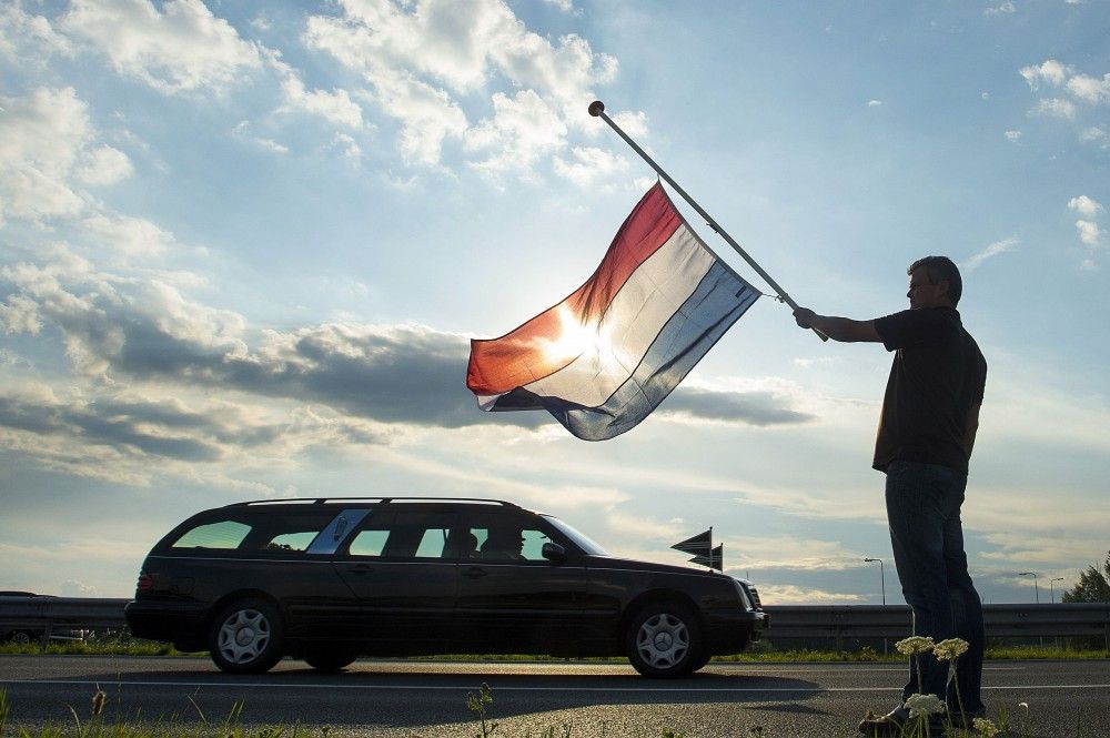 Dutch Ronald Visee holds a Netherlands flag flying at half-mast R as a hearse carrying the remains of the victims of the Malaysia Airlines flight MH17 plane disaster are escorted on highway A27 near Nieuwegein by military police, on their way to being i