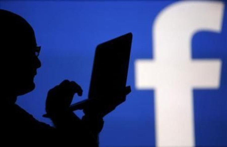 A man is silhouetted against a video screen with a Facebook logo 