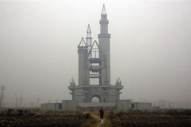 A farmer carries a shovel over his shoulder as he walks to tend his crops in a field that includes an abandoned building, that was to be part of an amusement park called &#039;Wonderland&#039;, on the outskirts of Beijing December 5, 2011. Construction wo