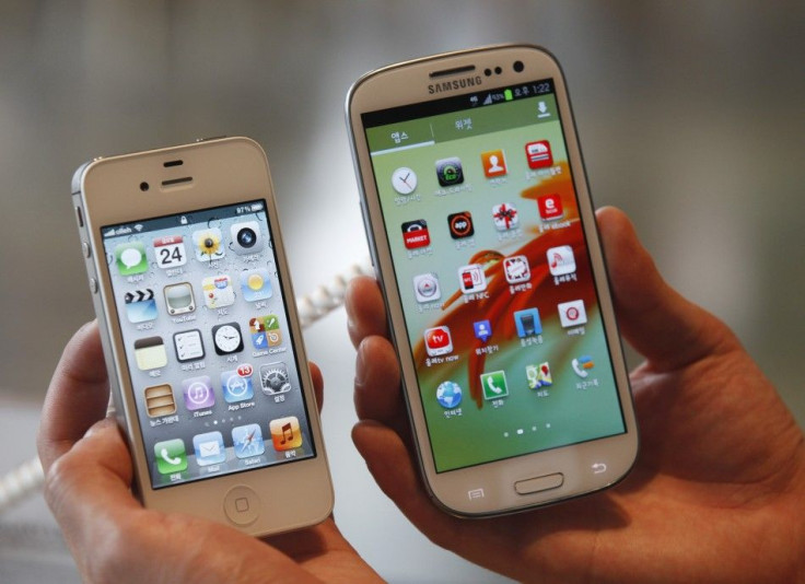 An Employee Poses As He Holds Apple's iPhone 4s (L) And Samsung's Galaxy S III At A Store In Seoul