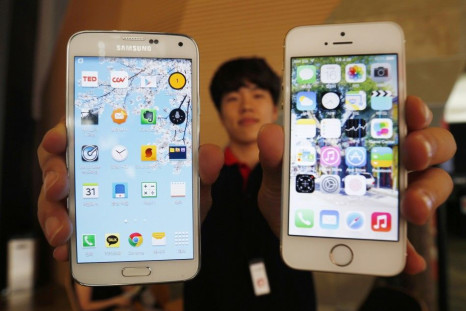A Sales Assistant Holding Samsung Electronics' Galaxy 5 Smartphone And Apple Inc's iPhone 5 Smartphone Poses For Photographs At A Store In Seoul