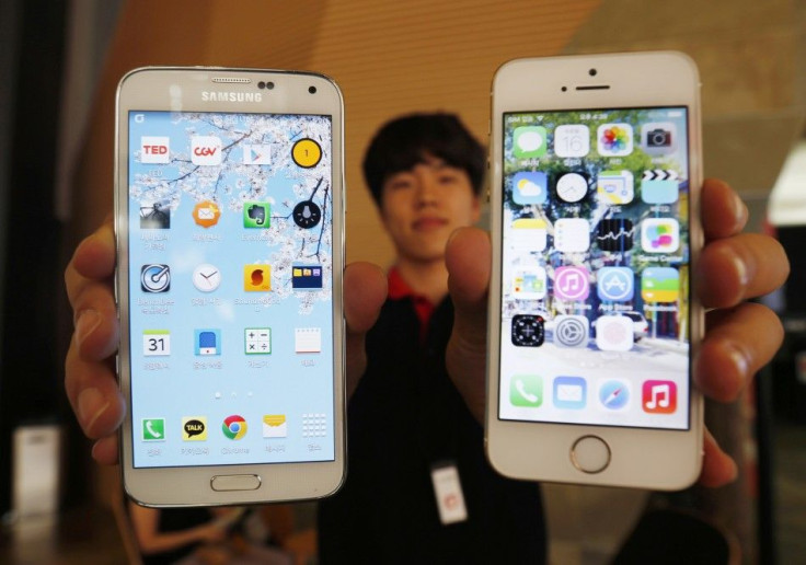 A Sales Assistant Holding Samsung Electronics' Galaxy 5 Smartphone And Apple Inc's iPhone 5 Smartphone Poses For Photographs At A Store In Seoul