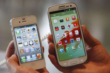 An employee poses as he holds Apple&#039;s iPhone 4s (L) and Samsung&#039;s Galaxy S III