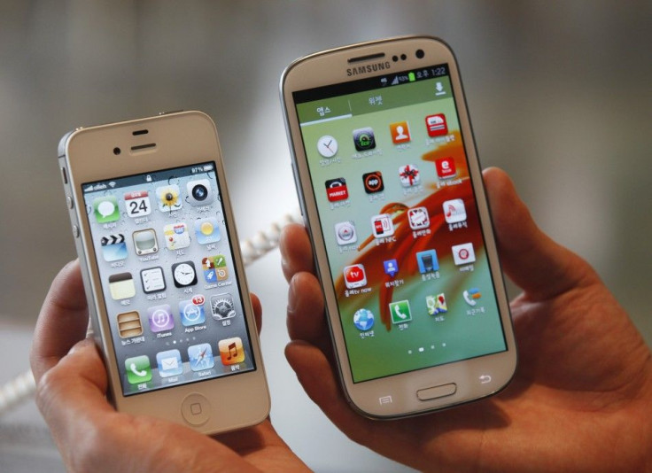 An employee poses as he holds Apple&#039;s iPhone 4s (L) and Samsung&#039;s Galaxy S III