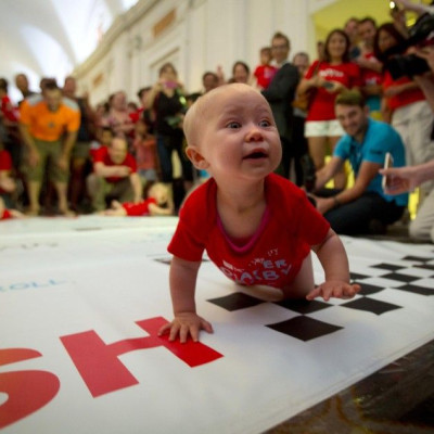 A baby looks to his mother as he crawls across the finish line