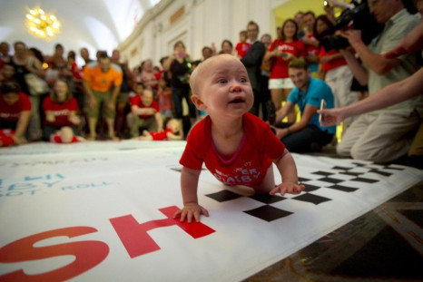 A baby looks to his mother as he crawls across the finish line